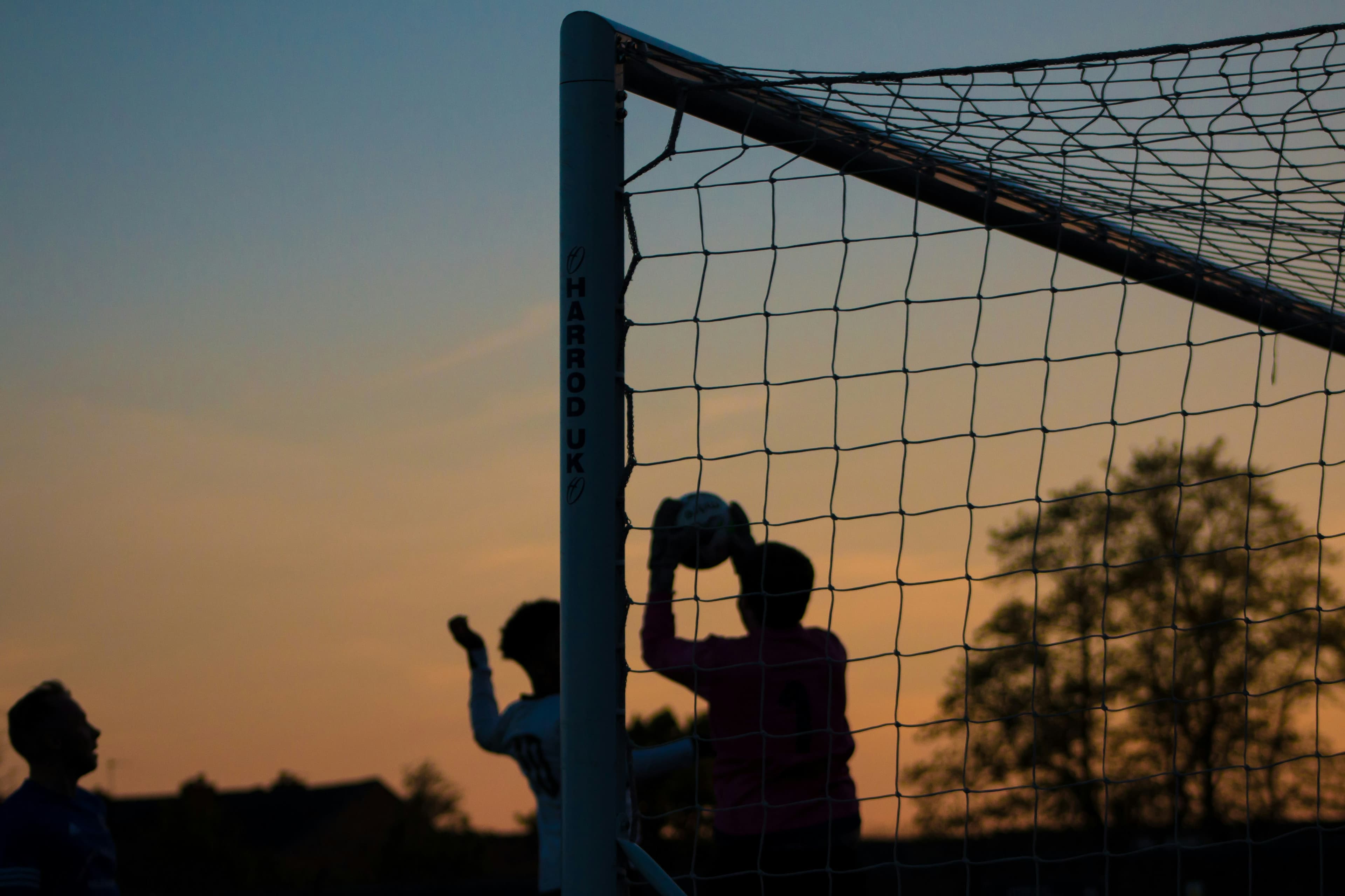 Keeper griper ballen i motlys ved solnedgang